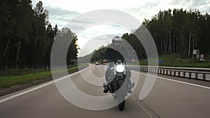 Man riding scrambler motorbike on the highway through the forest, front view