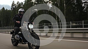 Man riding scrambler motorbike on the highway through the forest, side view