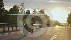 Man riding scrambler motorbike on the highway through the forest at the sunset