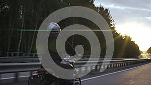 Man riding scrambler motorbike on the highway through the forrest at the sunset