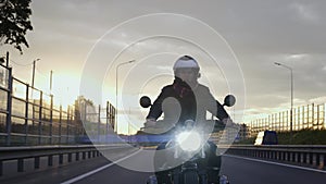 Man riding scrambler motorbike on the highway at the sunset, front view