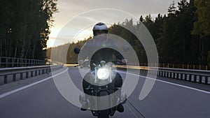 Man riding scrambler motorbike on the highway at the sunset, front view