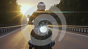 Man riding scrambler motorbike on the highway at the sunset, front view