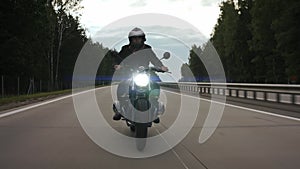 Man riding scrambler and turning on the highway through the forest, front view