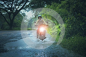 man riding small endurom motorcycle crossing shallow creek among rain falling at forest