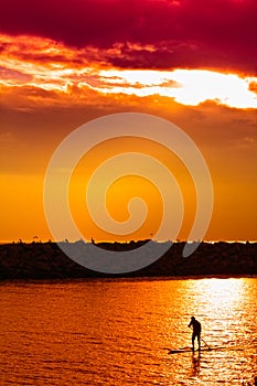 Man riding on a stand up paddle board SUP on a waterway under an orange sky.