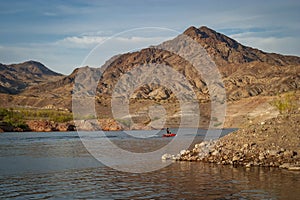 A man riding a watercraft on a desert lake with rocky hills and blue sky