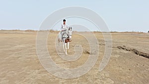 Man riding a white horse in an open field with a clear sky and desert in the background