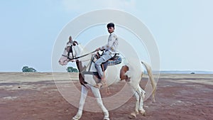 Man riding a white horse in an open field with a clear sky and desert in the background