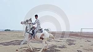 Man riding a white horse in an open field with a clear sky and desert in the background