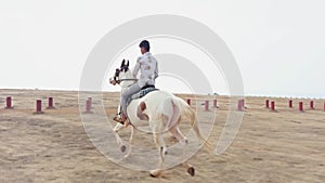 Man riding a white horse in an open field with a clear sky and desert in the background