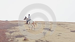 Man riding a white horse in an open field with a clear sky and desert in the background