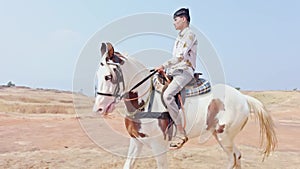 Man riding a white horse in an open field with a clear sky and desert in the background