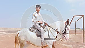 Man riding a white horse in an open field with a clear sky and desert in the background