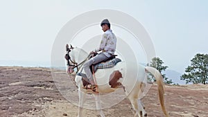 Man riding a white horse in an open field with a clear sky and desert in the background