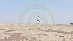 Man riding a white horse in an open field with a clear sky and desert in the background