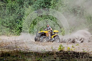 Man riding a yellow quad ATV all terrain vehicle on a sandy forest. Extreme sport motion, adventure, tourist attraction