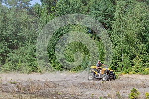 Man riding a yellow quad ATV all terrain vehicle on a sandy forest. Extreme sport motion, adventure, tourist attraction