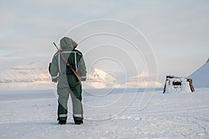 Man with a rifle looks out on the horizon in arctic landscape at Svalbard