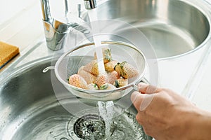 man rinses some white strawberries in a colander