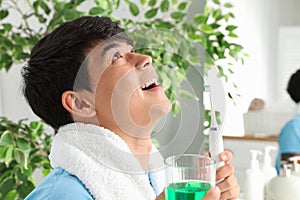 Man rinsing mouth with mouthwash in bathroom