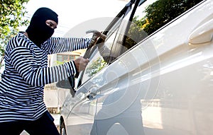 The man robber with a balaclava on his head holding a hammer trying to break into the car