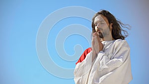 Man in robe praying to God against blue sky background, asking soul salvation