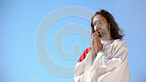 Man in robe praying to God against blue sky background, asking soul salvation