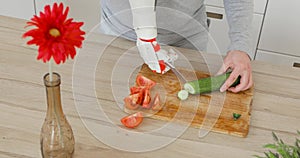 Man with robotic prosthetics hand with knife on it is cutting cucumber for salad on wooden board. Muscle reinnervation