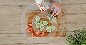 Man with robotic prosthetics hand with knife on it is trying to cut cucumber for slices on wooden board.