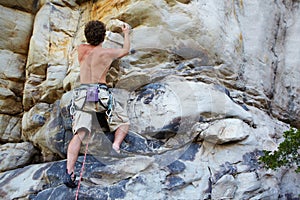 Man, rock climbing and rope hanging on mountain boulder for challenge, risk performance on stone. Male person, exercise