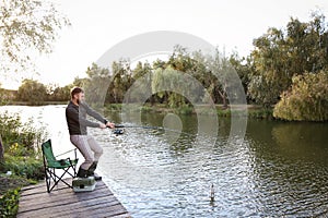 Man with rod fishing on wooden pier at riverside