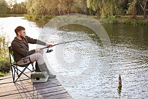 Man with rod fishing on wooden pier at riverside