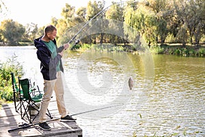 Man with rod fishing on wooden pier at riverside.