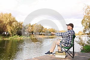 Man with rod fishing on wooden pier at riverside.