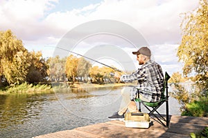 Man with rod fishing on wooden pier at riverside.