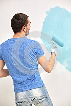 Man with roller painting wall in blue at home