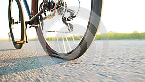A man rolls a bicycle with a punctured wheel on the asphalt against the backdrop of the summer sun, close-up. Slow