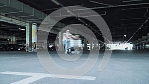 The man rolls the girl in the trolley from the supermarket in a circle in the underground parking