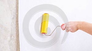 A man rolls out a canvas of white wallpaper with a suture yellow roller. Removing air bubbles and glue. Wallpapering.