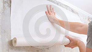 A man rolls out a roll of white wallpaper on the wall with glue. Wallpapering. Repair of room, apartment, house.