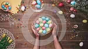 Man rotating basket with easter eggs on table decorated with easter eggs. Top view