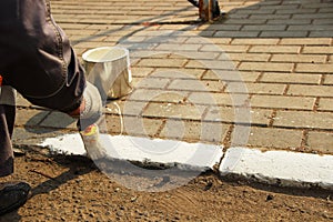 Man round brush paints white paint curbstone near the road, close-up