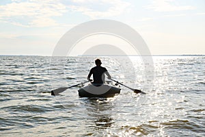 Man rowing inflatable rubber fishing boat on sea, back view