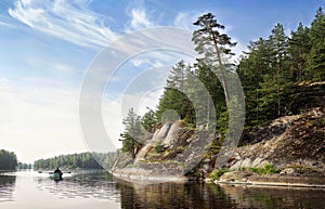 man rows on boat in nordic rocky bay. Big slanted pine on granite cliff. Baltic sea, gulf of Finland