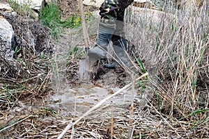 man in rubber boots digs a shovel pit in a swamp. Finding water