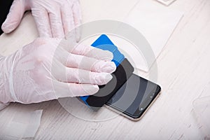 man in rubber gloves glues a protective glass to a smartphone using a special palstic spatula with a soft nozzle