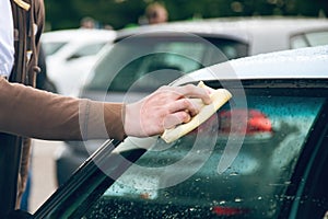 A man rubs a car windshield with a napkin. close-up
