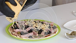 A man rubs cheese on a pizza. Cooking ingredients are laid out on it. Making pizza at home. Close-up shot