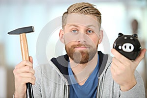 man with rueful expression holding hammer and piggybank